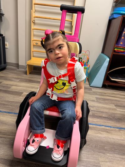 Girl is shown using a pink Toddler Mobility Trainer wearing a pink harness